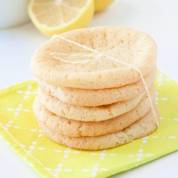 Lemon sugar cookies in a stack wrapped in twine on a yellow napkin with lemons in the background
