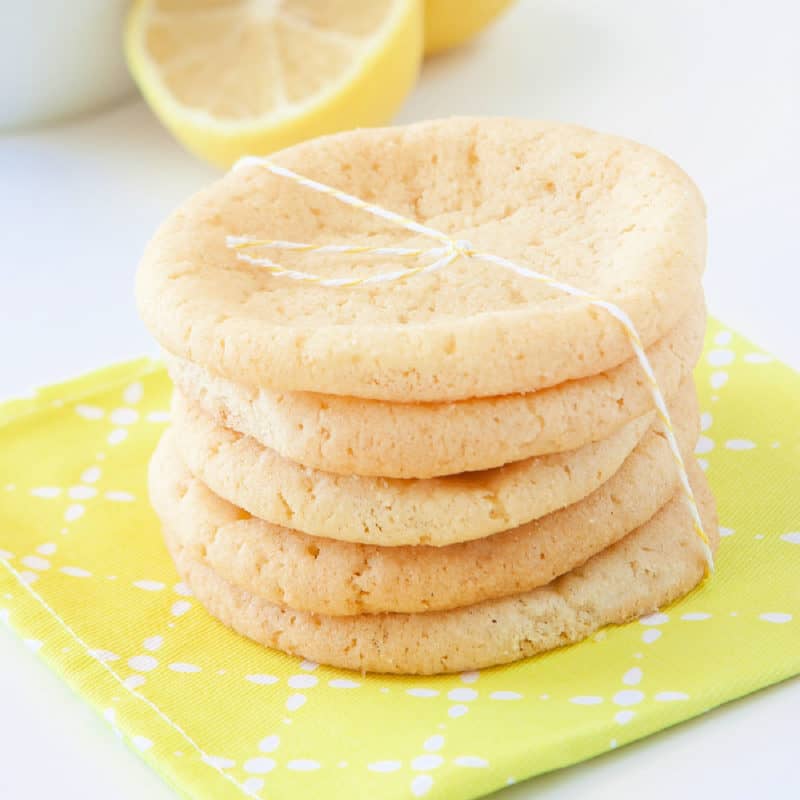 Lemon sugar cookies in a stack wrapped in twine on a yellow napkin with lemons in the background