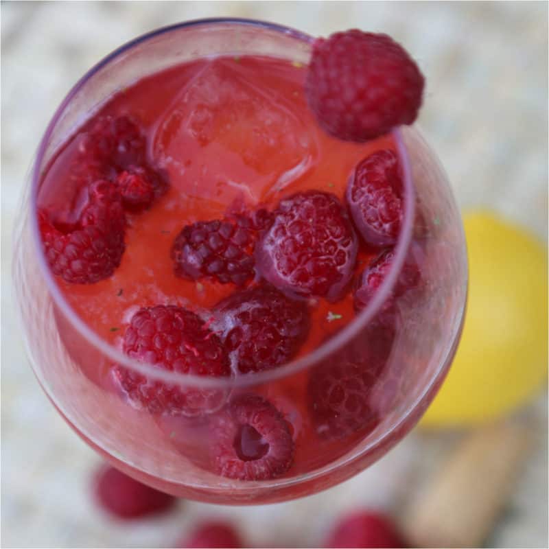 raspberries floating in a red cocktail in a wine glass
