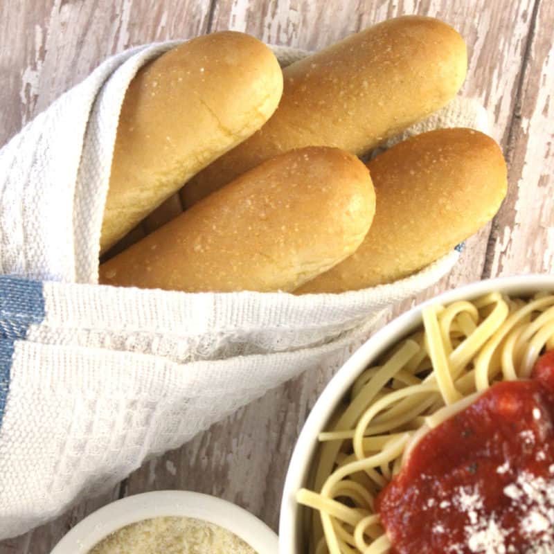 Olive Garden breadsticks wrapped in a cloth next to a bowl of spaghetti