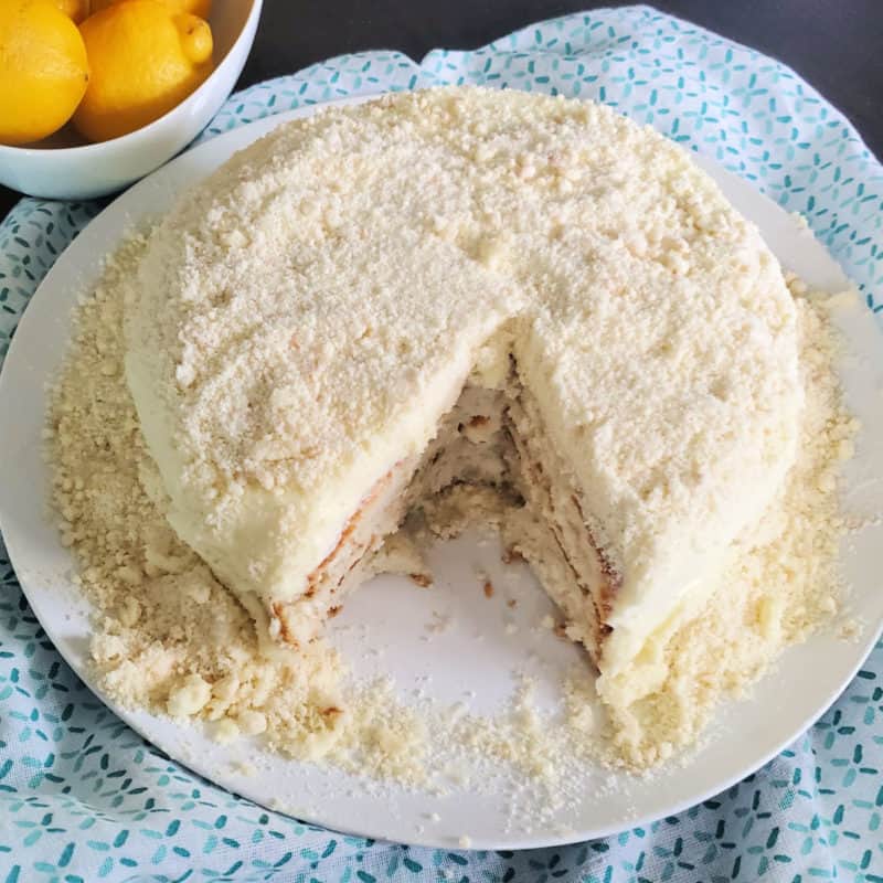 Lemon Cream Cake with a slice missing on a white plate next to a bowl of lemons