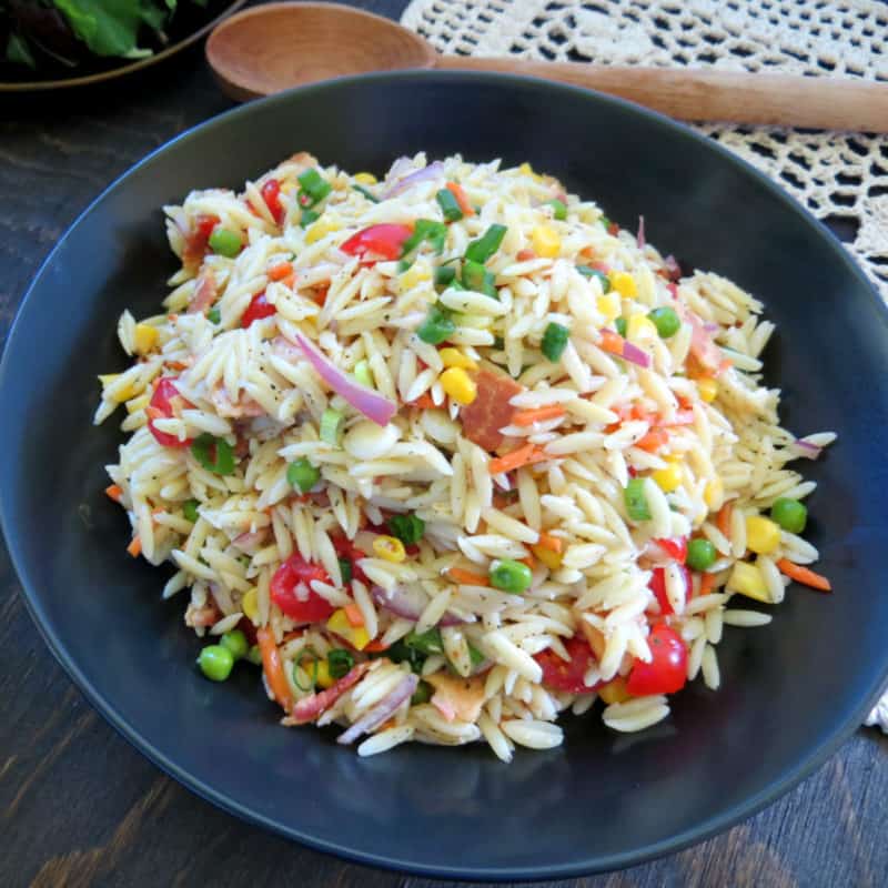 Orzo Pasta Salad on a blue plate next to a wooden spoon