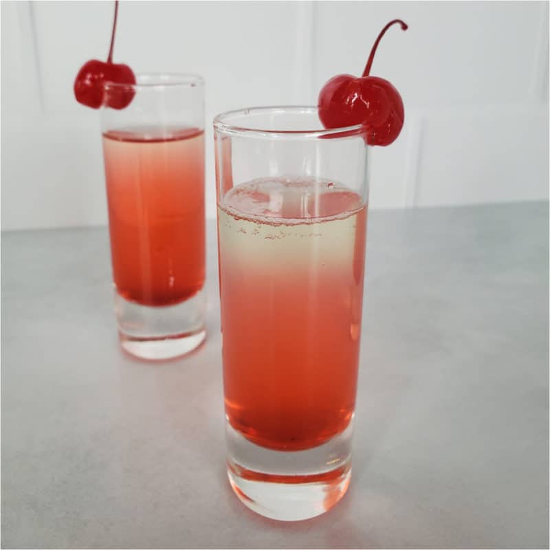 layered red cocktail garnished with cherries