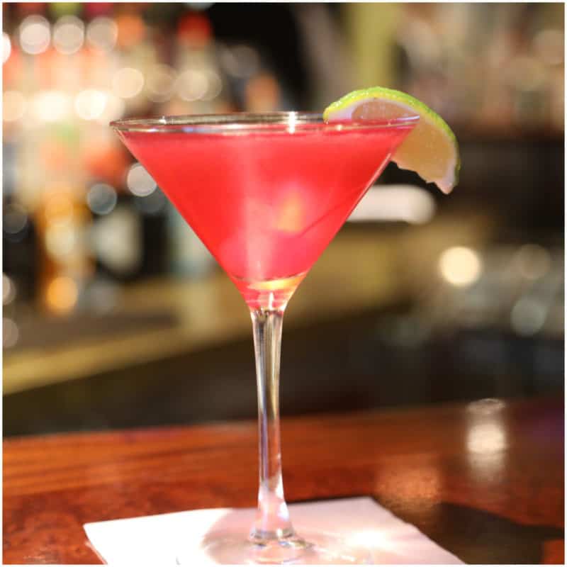 Bright red martini with a lime wedge in a martini glass on a white napkin