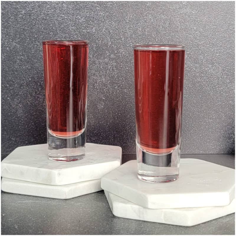 Two red cocktail shots on white coasters. 