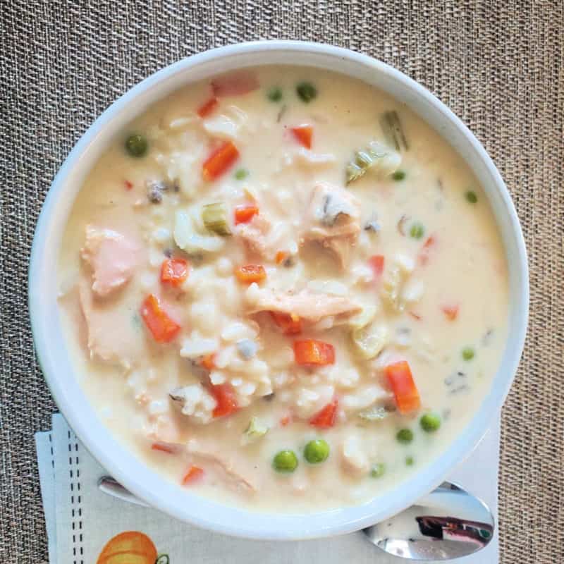 Turkey wild rice soup in a white bowl next to a silver spoon and napkin