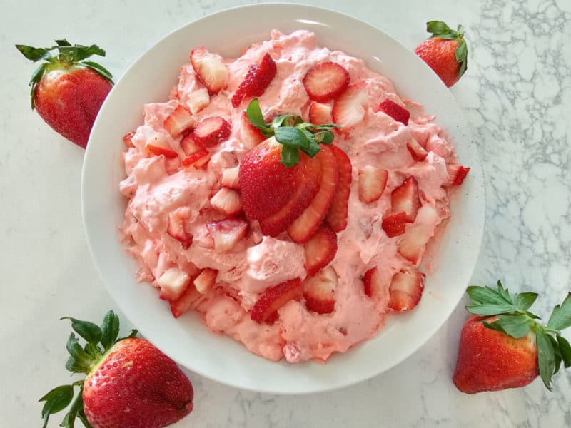 Strawberry fluff salad in a white bowl topped with fresh strawberries on a white counter