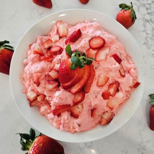 Strawberry fluff salad in a white bowl with cut strawberries for garnish