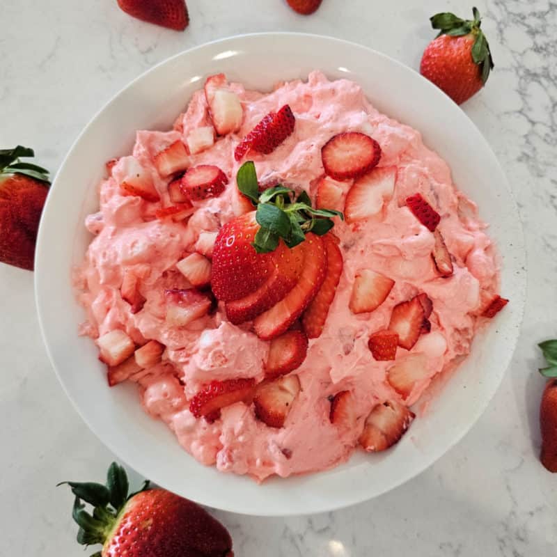 Strawberry fluff salad in a white bowl with cut strawberries for garnish