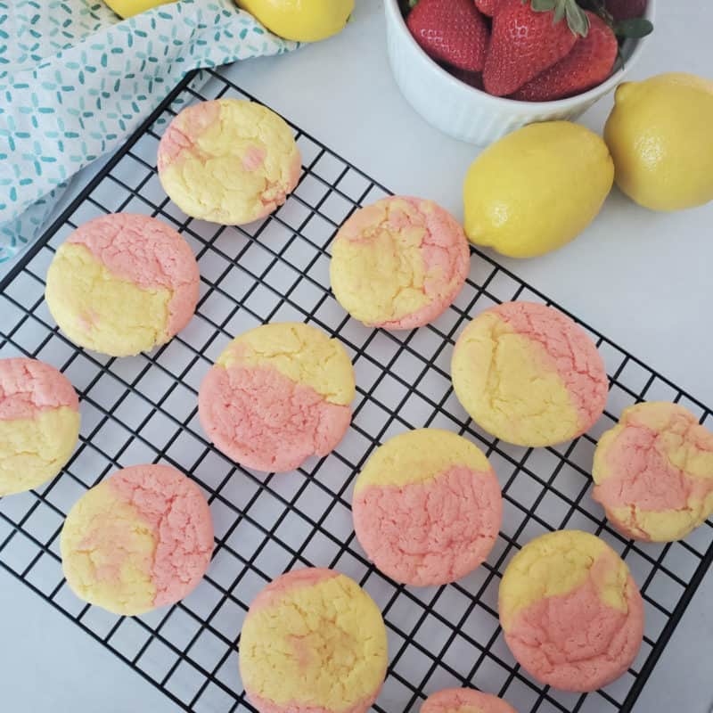 Strawberry Lemonade Cookies on a wire rack next to a bowl of strawberries and lemons