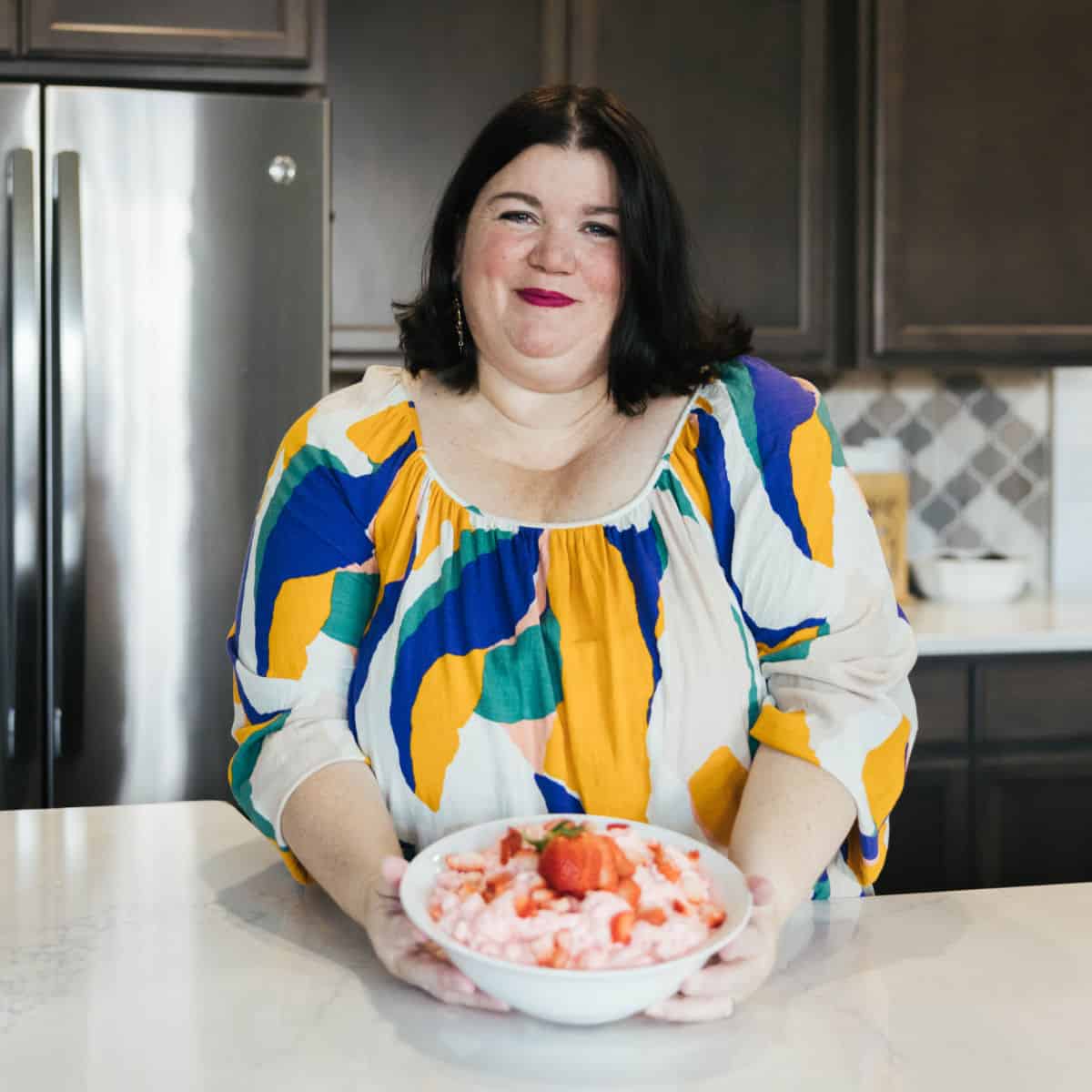 Tammilee holding a bowl of Strawberry Jello Fluff in home kitchen