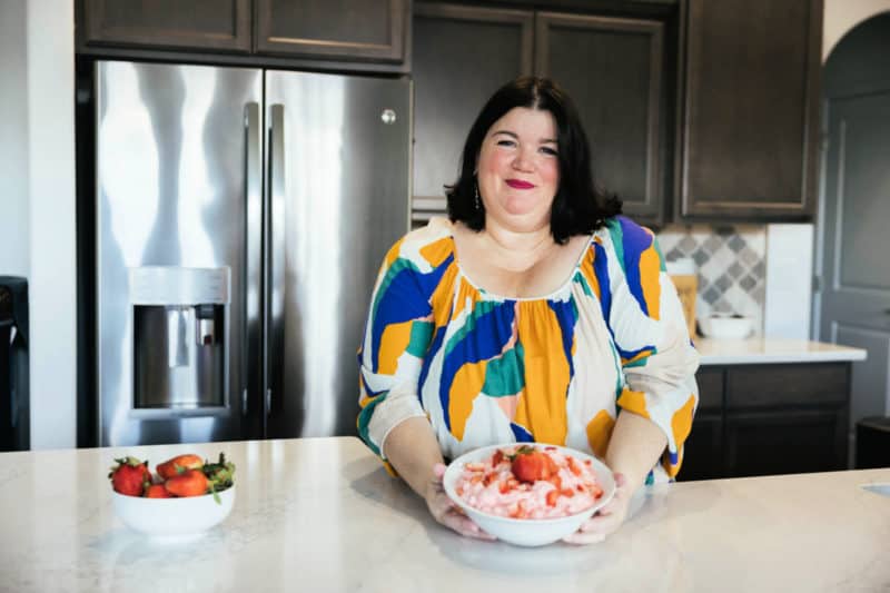 Tammilee holding a bowl of Strawberry Fluff in home kitchen next to a bowl of strawberries