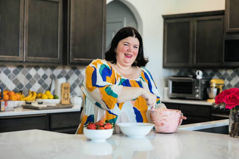 Tammilee making strawberry fluff salad in home kitchen with fruit on the back counter