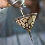 Tiramisu Martini pouring from a cocktail shaker into a martini glass with chocolate design.