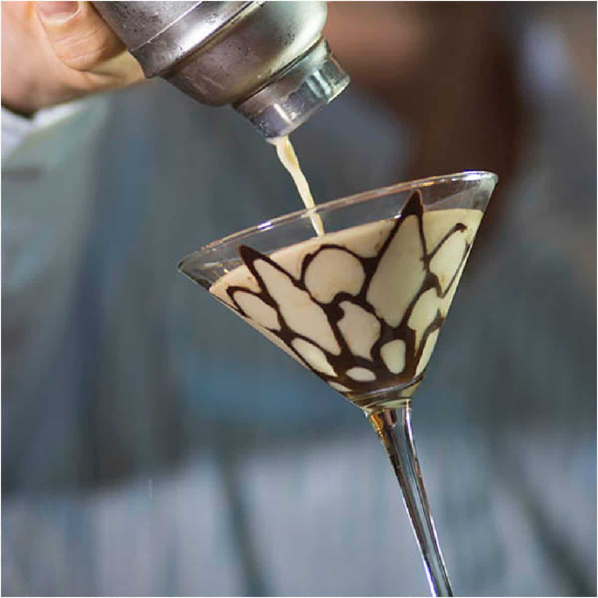 Tiramisu Martini pouring from a cocktail shaker into a martini glass with chocolate design.