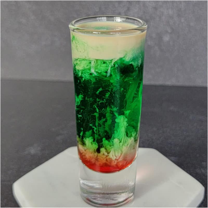 Cream Green and red Zombie Brain Shot in a clear shot glass on a white coaster.