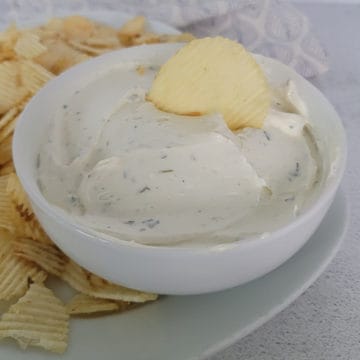 potato chip dip in a white bowl with a potato chip dipping into the dip, surrounded by more chips on a plate