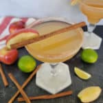 Apple Cider Margarita with a cinnamon stick surrounded by apples and lime wedges