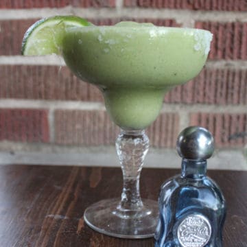 Avocado Margarita with a lime wedge next to a small bottle