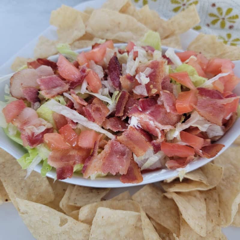 blt dip in a white bowl surrounded by tortilla chips