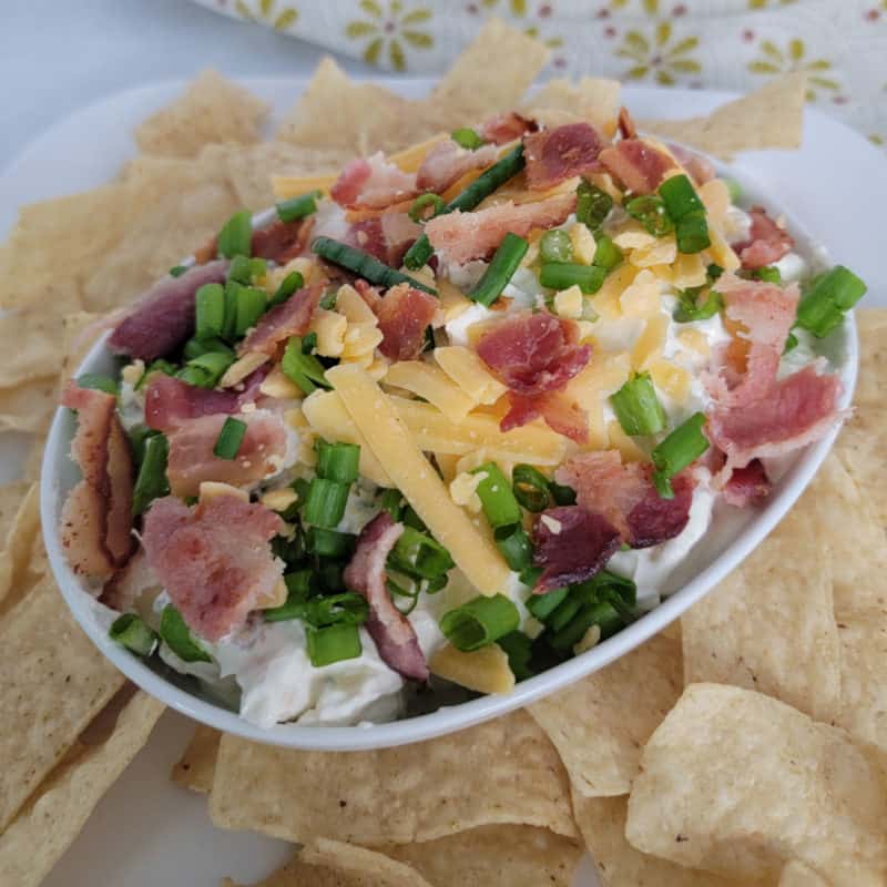 Bacon Cheddar Ranch Dip in a white bowl surrounded by tortilla chips