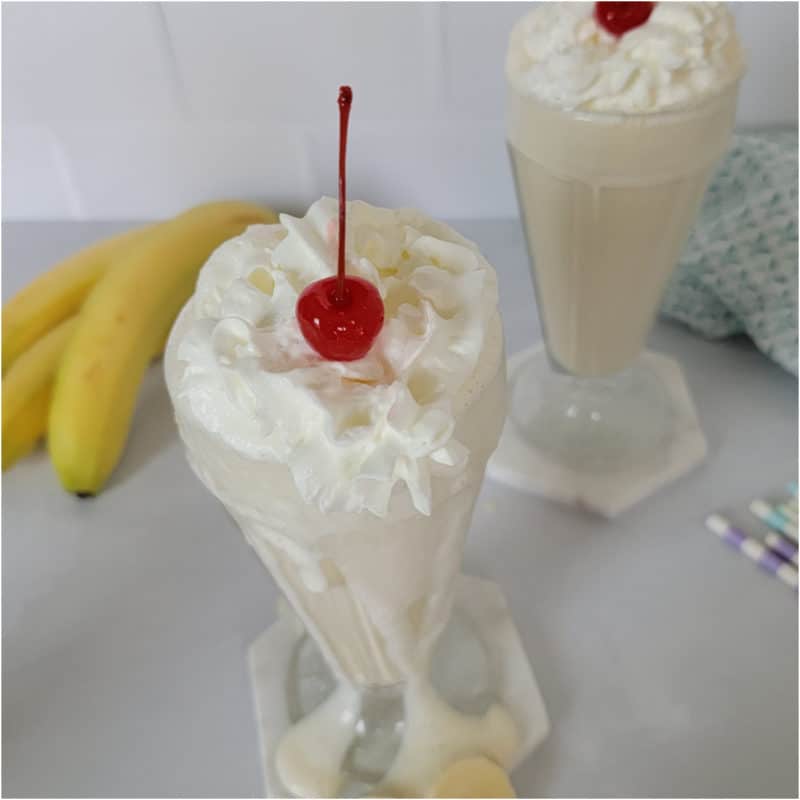 Banana milkshake with whipped cream and a cherry next to bananas and paper straws