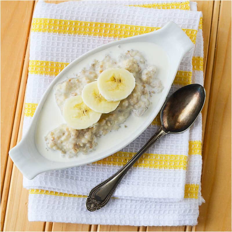 Banana Oatmeal in a long bowl next to a spoon on a white and yellow striped towel