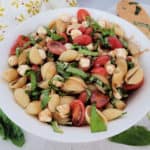 Caprese Pasta Salad in a white bowl next to a wooden spoon