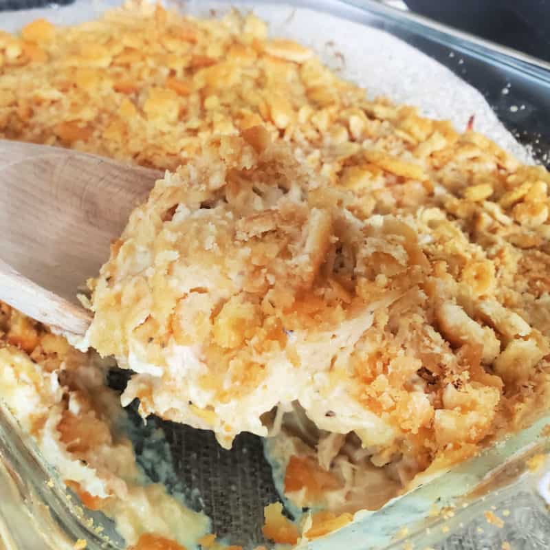 Ritz cracker topped chicken casserole in a glass dish with a wooden spoon