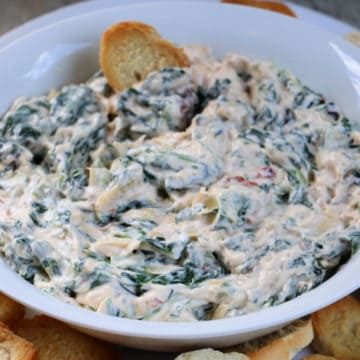 Creamy Spinach Artichoke Dip in a white bowl with a baguette