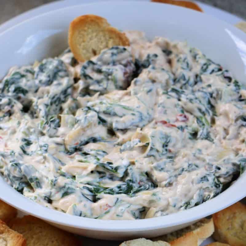 Creamy Spinach Artichoke Dip in a white bowl with a baguette 