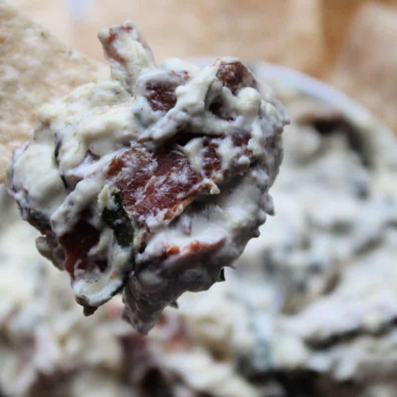 Bacon blue cheese dip on a tortilla chip above a white bowl