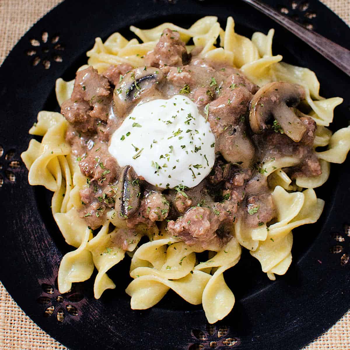 Beef stroganoff garnished with sour cream on a dark plate