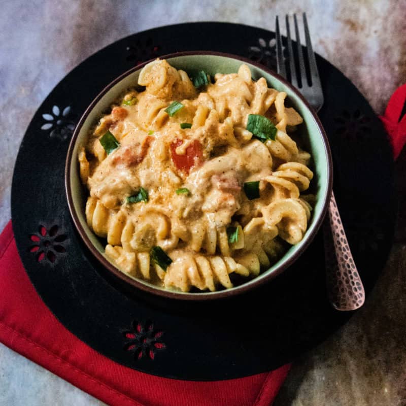 Mexican mac and cheese in a dark bowl next to a fork. 