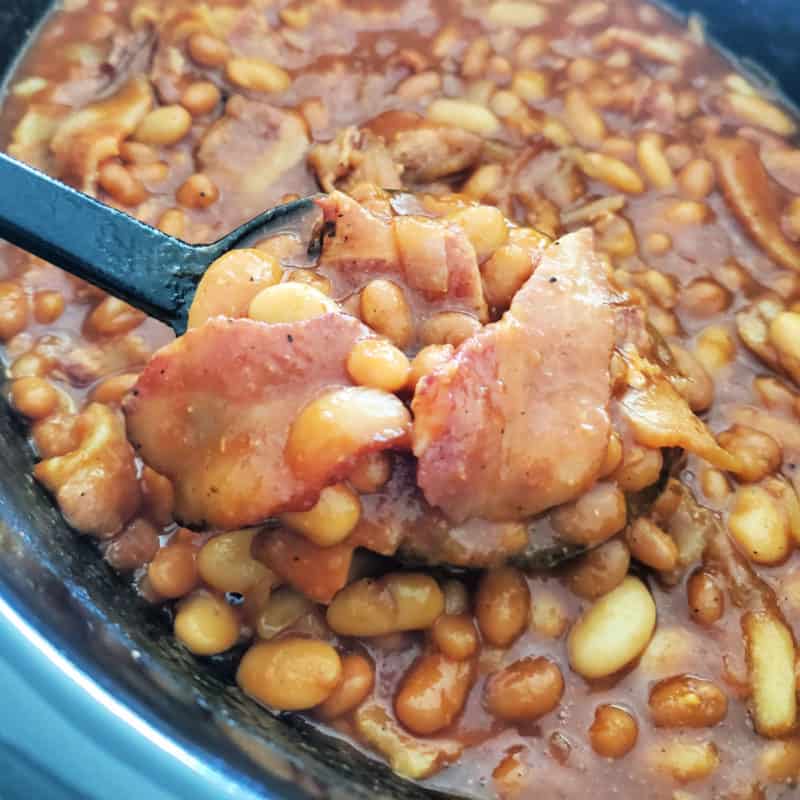 Baked Beans scooping out of a slower cooker with a black spoon