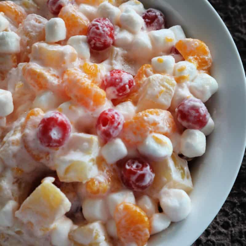 Fruit salad with mandarins, pineapples, mini marshmallows, and cherries in a white bowl