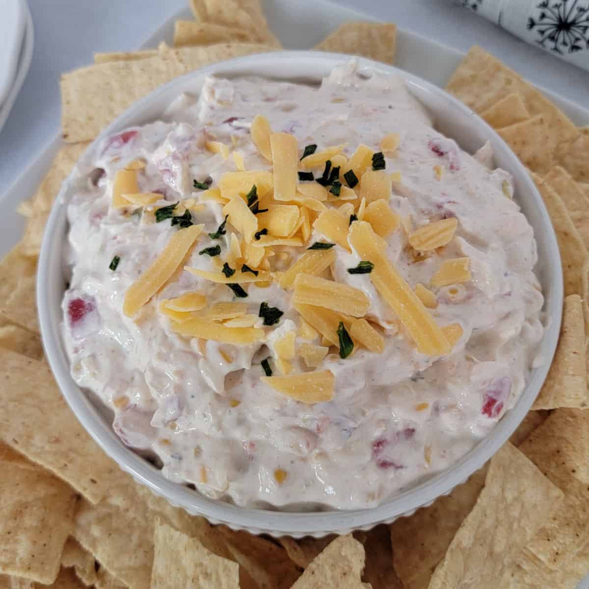 Fiesta Ranch Dip with shredded cheddar cheese garnish in a white bowl surrounded by tortilla chips