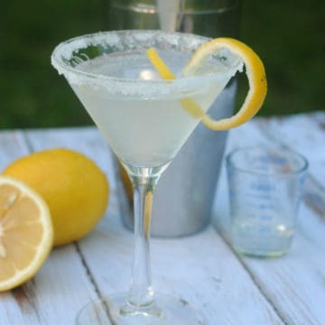 Lemon Drop Martini with sugared rim next to lemons and a cocktail shaker