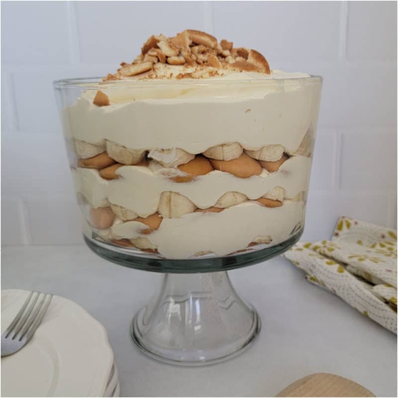 Magnolia Bakery Banana Pudding layered in a large trifle dish next to a stack of plates and cloth napkin