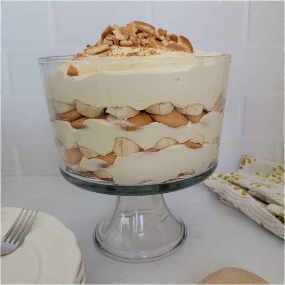 Magnolia Bakery Banana Pudding layered in a large trifle dish next to a stack of plates and cloth napkin