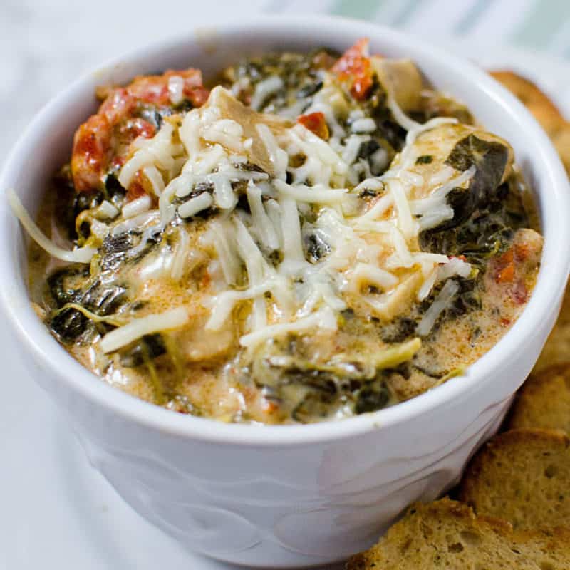 Slow Cooker Crock Pot Spinach Artichoke Dip With Sun-Dried Tomatoes in a white bowl with bread slices
