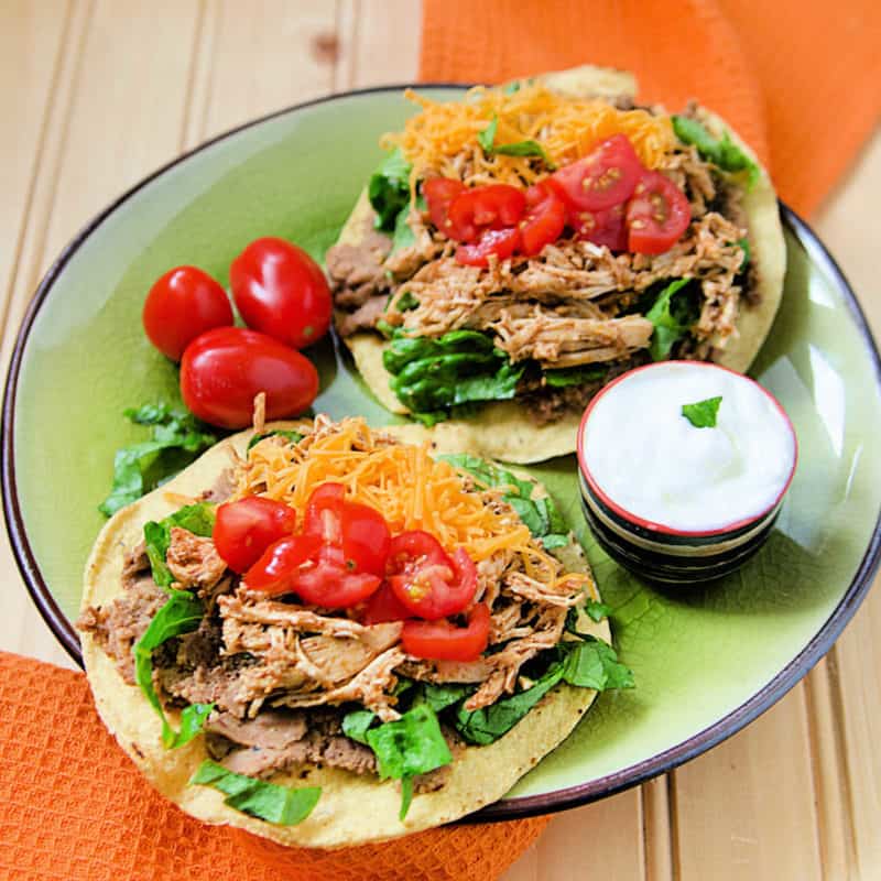 chicken tostadas topped with cheese and tomatoes on a green plate