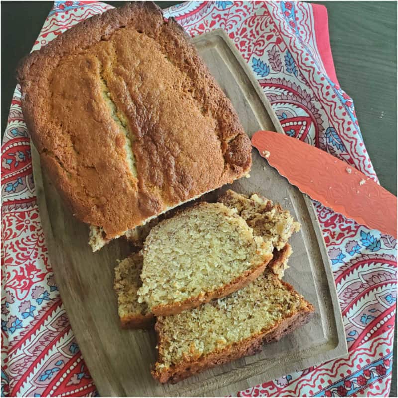Loaf of sour cream banana bread with slices cut on a wooden cutting board with knife and cloth napkin