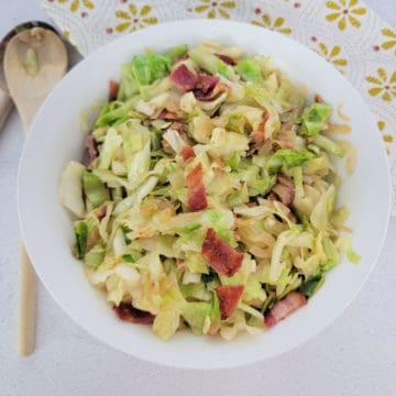 southern fried cabbage with bacon in a white bowl next to a wooden spoon