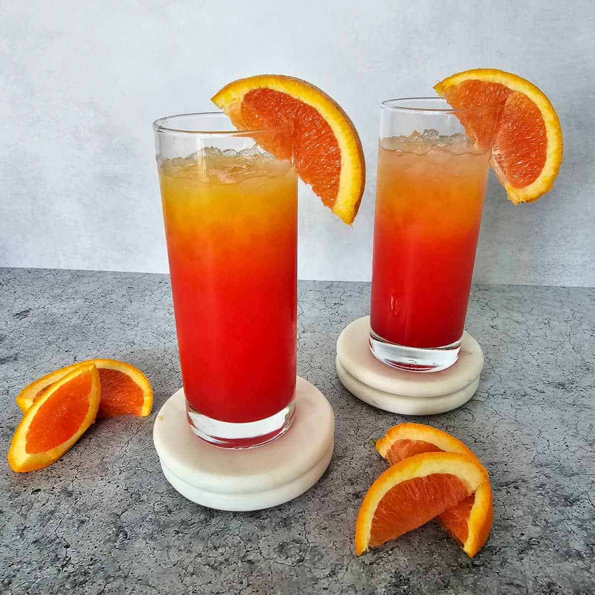 Two Vodka Sunrise Cocktails in tall glasses with orange wedges garnish