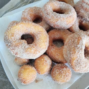 Biscuit Donuts piled on a white plate with cinnamon sugar