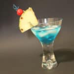 blue shark cocktail with pineapple wedge and cherry garnish in a martini glass