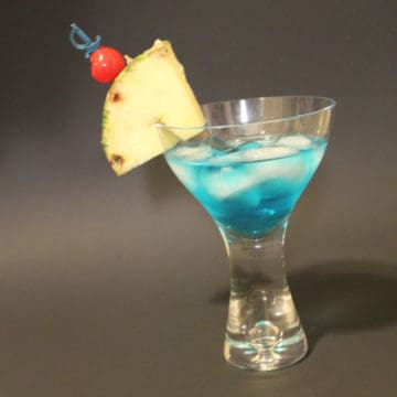 blue shark cocktail with pineapple wedge and cherry garnish in a martini glass