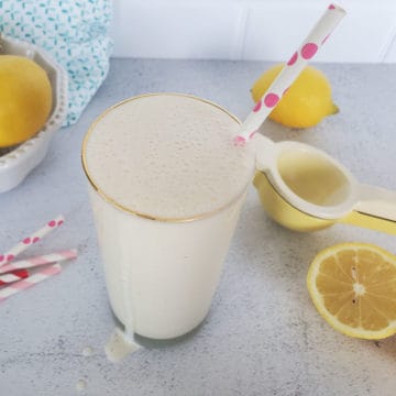 Frosted lemonade in a tall glass with a polka dot straw, surrounded by lemons