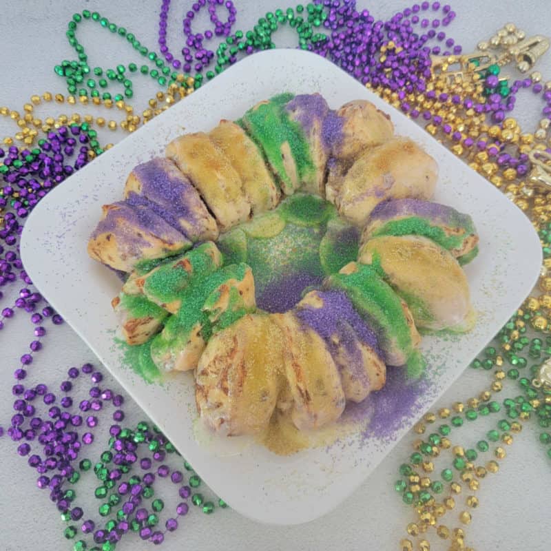 Cinnamon Roll King Cake on a white platter surrounded by Mardi Gras Beads